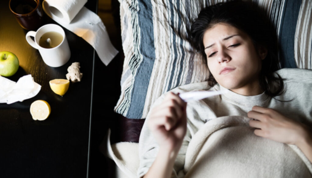 生病的年轻女子在家里的床上患流感，测量体温